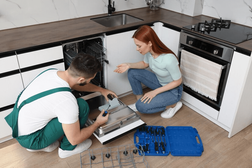 Woman looking how serviceman repairing her dishwasher in kitchen